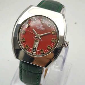 May include: A vintage Breitling Geneve automatic watch with a red dial and a date display at the 6 o'clock position. The watch has a silver-tone case and a green leather strap. The watch is displayed on a clear stand.