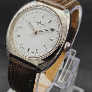 May include: A silver-tone wristwatch with a white dial, silver baton indices, and silver hands. The watch features the Ulysse Nardin logo with an anchor symbol at the twelve o'clock position and the text SWISS MADE at the bottom. It has a brown leather strap.
