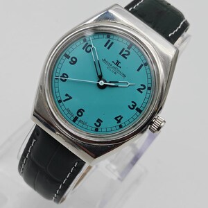 Pode incluir: Um rel&oacute;gio Jaeger-LeCoultre Club prateado com mostrador turquesa e algarismos pretos. Possui uma pulseira de couro preta com costura branca. O mostrador exibe o logotipo Jaeger-LeCoultre e "SWISS MADE".