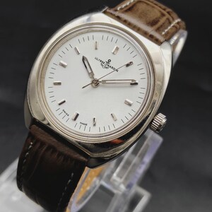 May include: A silver-tone wristwatch with a white dial, silver baton indices, and silver hands. The watch features the text Ulysse Nardin and an anchor logo below the twelve o'clock position, with Swiss Made at the bottom. It has a brown leather strap.