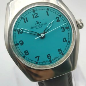 Op de afbeelding: Een zilverkleurig Jaeger-LeCoultre Club horloge met een turquoise wijzerplaat en zwarte cijfers. Het heeft een bruine leren band en de tekst "SWISS MADE".