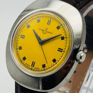 May include: A vintage Ulysse Nardin wristwatch with a bright yellow face and black hands. The watch has a silver-coloured case and a dark brown leather strap. The watch face features black rectangular hour markers and the words "Ulysse Nardin" and "Swiss Made".