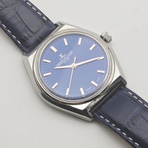 May include: A silver-toned wristwatch with a blue face and a navy blue leather band. The watch face features silver-toned hour markers and hands. The band is stitched with white thread. The watch is a classic timepiece.