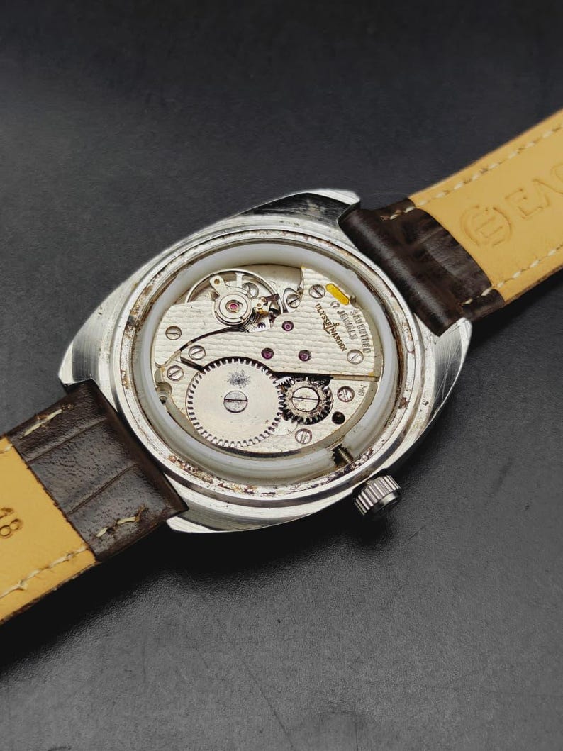 May include: A silver-toned wristwatch with the back casing removed to reveal the internal mechanical movement. The movement is marked Ulysse Nardin 17 Jewels. The watch features a brown leather strap with a light-colored underside.