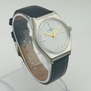 May include: A silver-toned wristwatch with a white face and gold hands and markers. The watch has a black leather band. The watch face has the words "ULYSSSE NARDIN" printed on it.