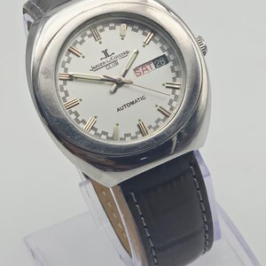 Puede incluir: Un reloj autom&aacute;tico Jaeger-LeCoultre Club plateado con esfera blanca, correa de cuero negro y fecha mostrada como S&Aacute;B 28. El reloj tiene una esfera redonda y una correa texturizada.