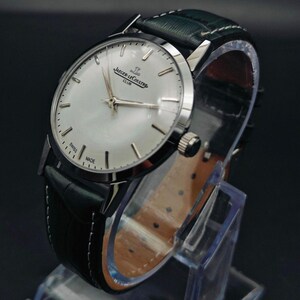 Pu&ograve; includere: Un orologio Jaeger-LeCoultre Club argentato con quadrante bianco e cinturino in pelle nera. L'orologio presenta lancette e indici argentati, con la scritta "SWISS MADE" sul quadrante. Il cinturino &egrave; largo circa 2 cm.