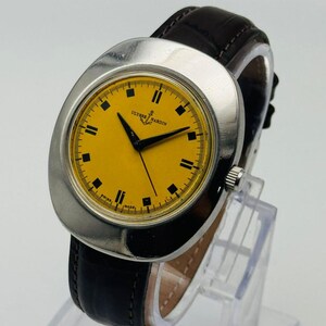 May include: A vintage Ulysse Nardin wristwatch with a bright yellow face and black hands. The watch has a silver-coloured case and a dark brown leather strap. The watch face has black square hour markers and the words "Ulysse Nardin" are printed on the face.