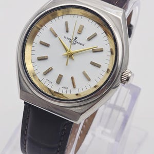 Pu&ograve; includere: Un orologio Ulysse Nardin vintage con cassa color argento, quadrante bianco con dettagli dorati e cinturino in pelle marrone. Il quadrante dell'orologio presenta lancette e indici dorati. L'orologio &egrave; marcato "SWISS MADE".