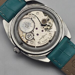 Peut inclure: Une montre-bracelet vintage ouverte, r&eacute;v&eacute;lant les m&eacute;canismes internes. Le bo&icirc;tier argent&eacute; entoure les engrenages, les ressorts et les bijoux du m&eacute;canisme. Le bracelet est en cuir turquoise.