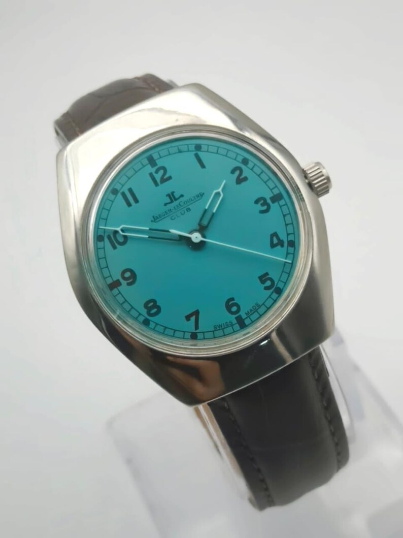 Op de afbeelding: Een vintage Jaeger-LeCoultre Club horloge met een turquoise wijzerplaat en zilveren kast. Het horloge heeft zwarte cijfers, zilveren wijzers en een bruine leren band. Het horloge is gemarkeerd met "Swiss Made".