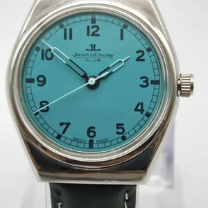 Pode incluir: Um rel&oacute;gio de pulso prateado com mostrador turquesa e algarismos pretos. O rel&oacute;gio apresenta a marca "JAEGER-LECOULTRE CLUB" e tem uma bracelete de couro verde escuro. Os ponteiros s&atilde;o prateados e o rel&oacute;gio est&aacute; marcado "SWISS MADE".