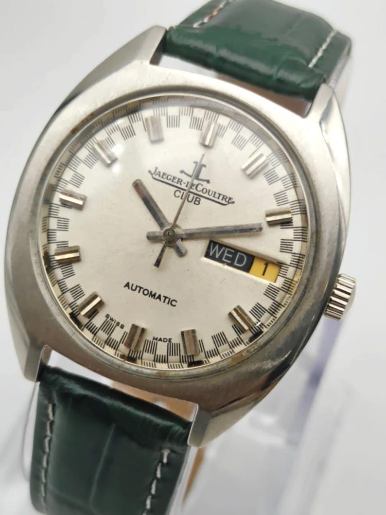 Puede incluir: Un reloj de pulsera autom&aacute;tico Jaeger-LeCoultre Club plateado con esfera blanca y correa de cuero verde. La esfera muestra el d&iacute;a de la semana. El reloj tiene agujas e indicadores plateados. Dise&ntilde;o cl&aacute;sico.