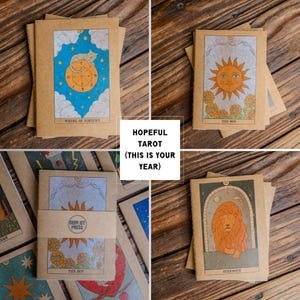 May include: A collection of tarot cards with illustrations of the Wheel of Fortune, the Sun, and Strength. The cards are printed on kraft paper and feature colorful designs. The text "HOPEFUL TAROT (THIS IS YOUR YEAR)" is also visible.