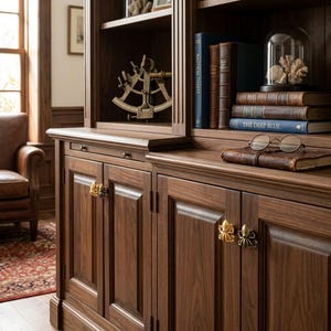 Puede incluir: Un mueble de madera oscura con cuatro pomos de latón en forma de pulpo. La superficie del mueble sostiene una pila de libros, una campana de cristal con un coral blanco, unas gafas redondas y un sextante de latón en el estante superior.