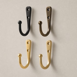 May include: Four metal wall hooks arranged in a two-by-two grid. Each hook features a curved J-shape with a ball tip and a flat mounting plate with two circular screw holes. The finishes include matte black, antique bronze, polished gold, and brass.