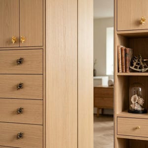 May include: A light oak wood cabinet featuring a series of drawers and open shelving. The drawers are adorned with metallic gold-toned shell-shaped knobs. The open shelves contain several vintage books and a glass cloche displaying seashells.