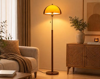 Könnte beinhalten: Eine Stehlampe mit einem hohen, schlanken Ständer aus dunklem Holz, einem runden Fuß und einem Hals aus poliertem Metall. Die Lampe hat einen halbkugelförmigen, leuchtend orangefarbenen Glasschirm, der ein warmes Licht abgibt und per Zugschalter bedient wird.