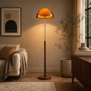 Könnte beinhalten: Eine Stehlampe mit einem kuppelförmigen orangefarbenen Glasschirm, einem schlanken Metallstab und einem dunklen Holzfuß. Die Lampe verfügt über einen Zugschalter und strahlt ein warmes, nach unten gerichtetes Licht aus, stehend auf einem runden Sockel.