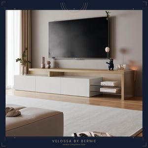 Peut inclure: Un meuble TV long et bas avec une finition en bois clair et trois portes d'armoire blanches. L'unité comprend des étagères en verre ouvertes sur le côté droit, contenant deux livres, et une surface supérieure plane supportant un téléviseur.