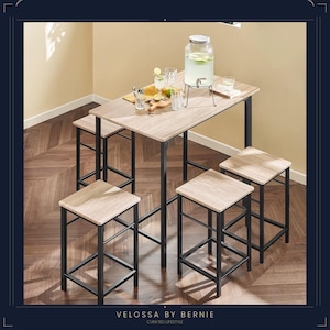 Op de afbeelding: Een bartafel in lichte houttint met vier bijpassende krukken. De tafel en krukken hebben zwarte metalen frames. Op de tafel staat een grote glazen drankdispenser, samen met glazen en een houten snijplank. De tafel is 101 cm lang.