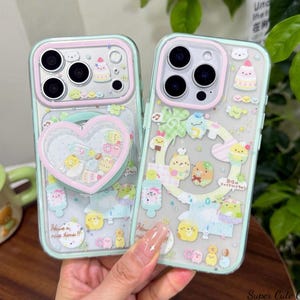 Peut inclure: Deux coques de téléphone transparentes avec une bordure vert menthe, décorées de personnages de dessins animés et de motifs aux couleurs pastel. L'une des coques a un support en forme de cœur. Le texte "Have a nice time!!" est visible.
