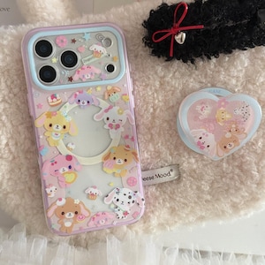 May include: A clear phone case with a light purple border, decorated with cartoon puppies, stars, and cakes. The case has a clear center and is next to a heart-shaped phone grip with similar puppy designs.
