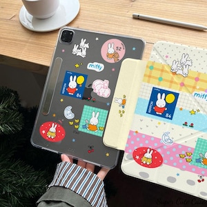 May include: A clear iPad case adorned with colorful Miffy stickers. The stickers feature the Miffy bunny character in various poses, along with the text "miffy" and the number "84". The case is paired with a matching patterned cover.