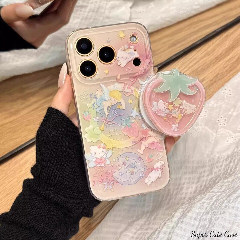 May include: A clear phone case with a colorful, whimsical design featuring cartoon characters, stars, and strawberries. A pink strawberry-shaped phone grip is attached. The text "Super Cute Case" is visible.