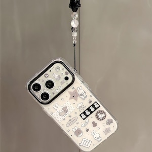 Pode incluir: Capa de telefone transparente com um design de coelho branco e preto. A capa tem uma borda preta para a c&acirc;mera e uma al&ccedil;a decorativa com contas pretas e brancas. O texto "Super Cute Case" &eacute; vis&iacute;vel.
