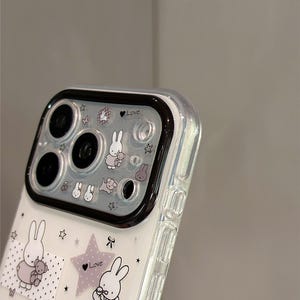 Pode incluir: Capa de telefone transparente decorada com coelhos de desenho animado, estrelas e a palavra "Love" em uma estrela roxa. A capa tem uma borda preta para a c&acirc;mera e o texto "Super Cute Case" no canto inferior direito.
