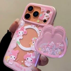 May include: Pink phone case with a clear back and a pop-up grip. The case features cartoon characters and a clear, pink grip filled with small figures. The text "Super Cute Case" is visible on the bottom right.