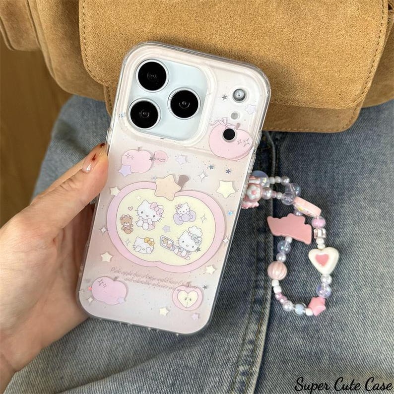 May include: Clear phone case with a pink apple design featuring Hello Kitty characters and stars. The case has a beaded wrist strap with pink and white accents. The text "Super Cute Case" is visible at the bottom right.