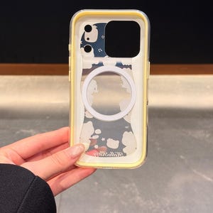 Peut inclure: Coque de t&eacute;l&eacute;phone transparente avec un bord jaune. La coque pr&eacute;sente un cercle blanc et un motif de nuages blancs et d'&eacute;toiles sur fond bleu. Le texte "Hello Kitty" est visible en bas.