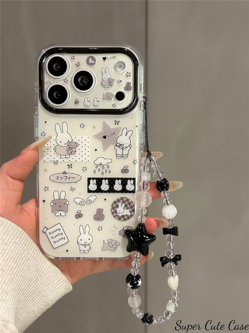 Pode incluir: Capa de telefone transparente com interior branco com coelhos de desenho animado, estrelas e a palavra "Love". Uma al&ccedil;a de contas com estrela preta, la&ccedil;os e contas est&aacute; presa. A capa tem o texto "Super Cute Case."