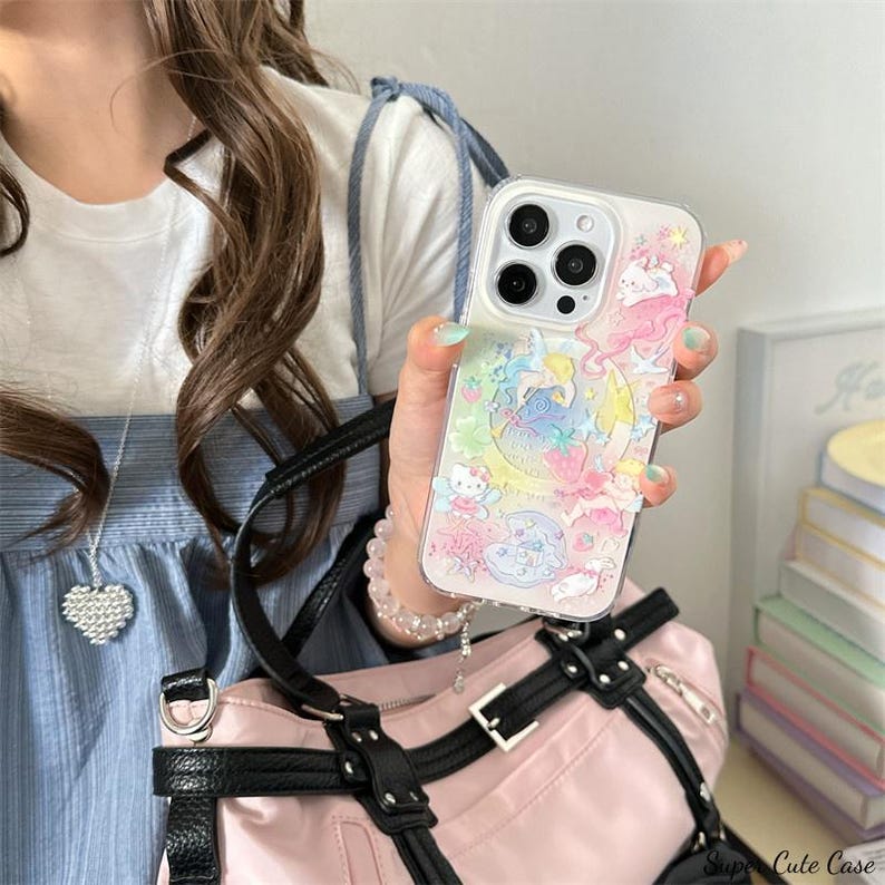 May include: Clear phone case with a colorful design featuring cartoon characters, a crescent moon, and stars. The case has a raised, textured design and is held in a hand. The phone case is a cute accessory.