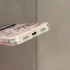Pode incluir: Capa de telefone transparente com fundo branco e pequenas ilustra&ccedil;&otilde;es pretas. A capa tem uma borda transparente. O texto "Super Cute Case" &eacute; vis&iacute;vel no canto inferior direito.