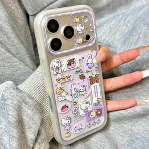 May include: A clear phone case with a purple border and a variety of cartoon character stickers. The stickers include Hello Kitty, bears, bunnies, and other cute designs. The case has a camera cutout and the text "Super Cute Case".