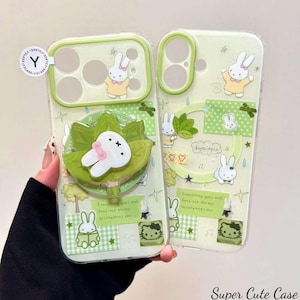May include: Two light green phone cases with a bunny theme. One case has a 3D bunny pop-up grip. Both cases feature bunny illustrations, text, and decorative elements in green and white. The text on the case says "Everything goes well. Good luck always accompanies you."