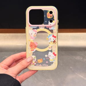 Peut inclure: Une coque de t&eacute;l&eacute;phone transparente avec un bord jaune et un motif Hello Kitty. La coque pr&eacute;sente divers personnages et aliments Hello Kitty. Le texte "Hello Kitty" est visible sur la coque.