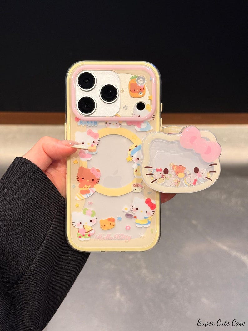 Peut inclure: Une coque de t&eacute;l&eacute;phone jaune avec une bordure rose et un pop-socket assorti. La coque pr&eacute;sente des personnages Hello Kitty et d'autres illustrations mignonnes. Le pop-socket a un design de n&oelig;ud rose. Le texte "Hello Kitty" est visible.