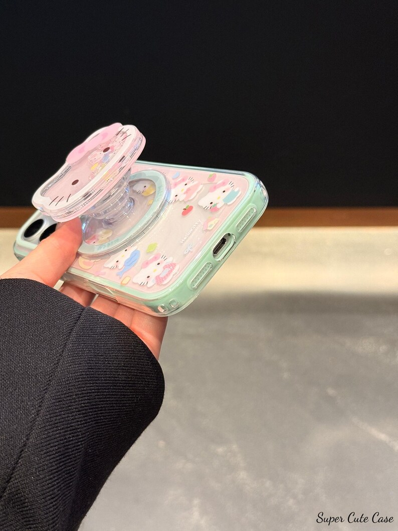 May include: A clear phone case with a pink and mint green design featuring cartoon bunnies and strawberries. The case has a pop-up grip with a pink bow and a cartoon cat face. The words "Super Cute Case" are visible in the bottom right corner.