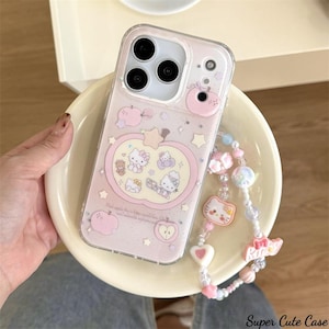 May include: A clear phone case with a pink apple design featuring Hello Kitty characters. The case has a beaded charm strap with pink, white, and blue beads and charms. The text "Super Cute Case" is at the bottom right.
