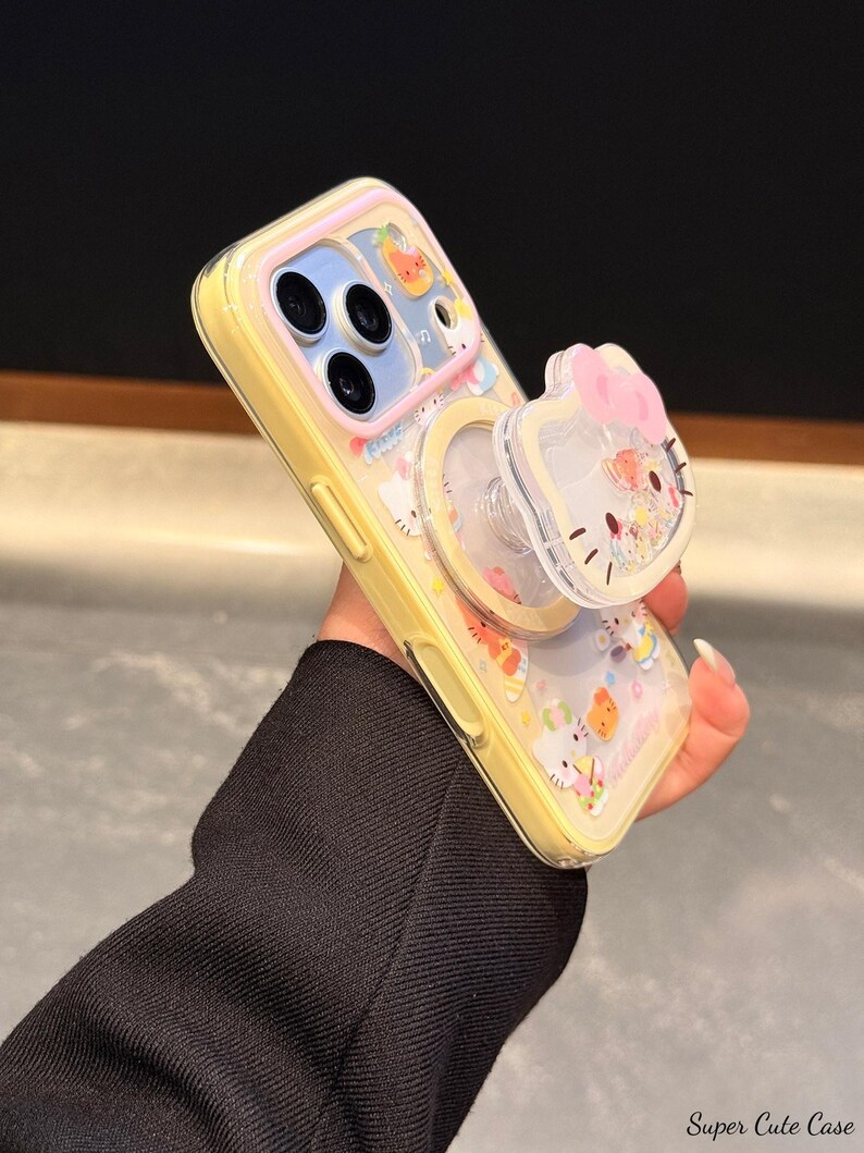 Peut inclure: Coque de t&eacute;l&eacute;phone jaune avec un dos transparent orn&eacute; d'un motif de dessin anim&eacute; et d'une poign&eacute;e pop-up. La poign&eacute;e pop-up a la forme d'un personnage avec un n&oelig;ud rose. La coque a une bordure jaune et un dos transparent avec des graphiques de dessins anim&eacute;s.