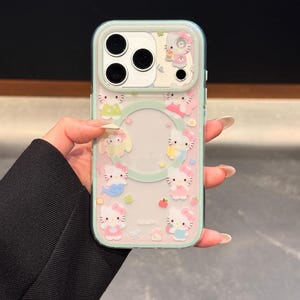 May include: Clear phone case with a mint green border and a repeating pattern of Hello Kitty characters in various outfits. The case has a clear center with a circular cutout for the phone's logo.