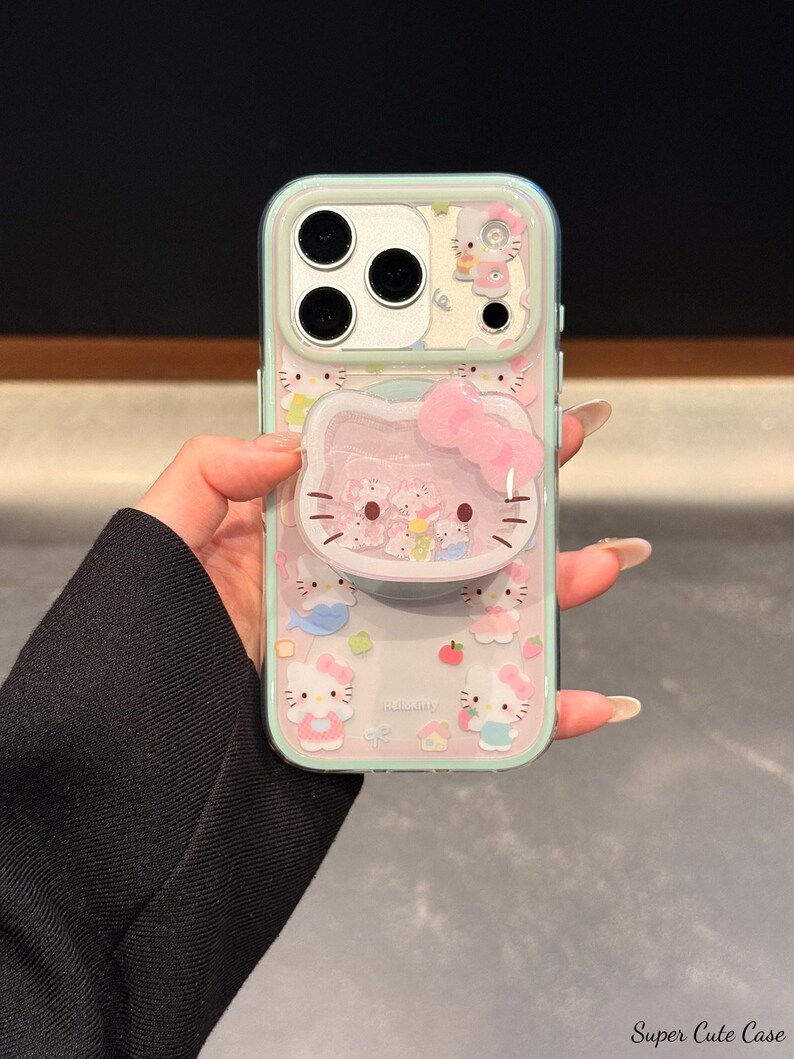 May include: A clear phone case with a mint green border featuring a Hello Kitty design. The case has a 3D Hello Kitty face with a pink bow and a pop-up feature. The background is filled with Hello Kitty characters and other cute graphics.
