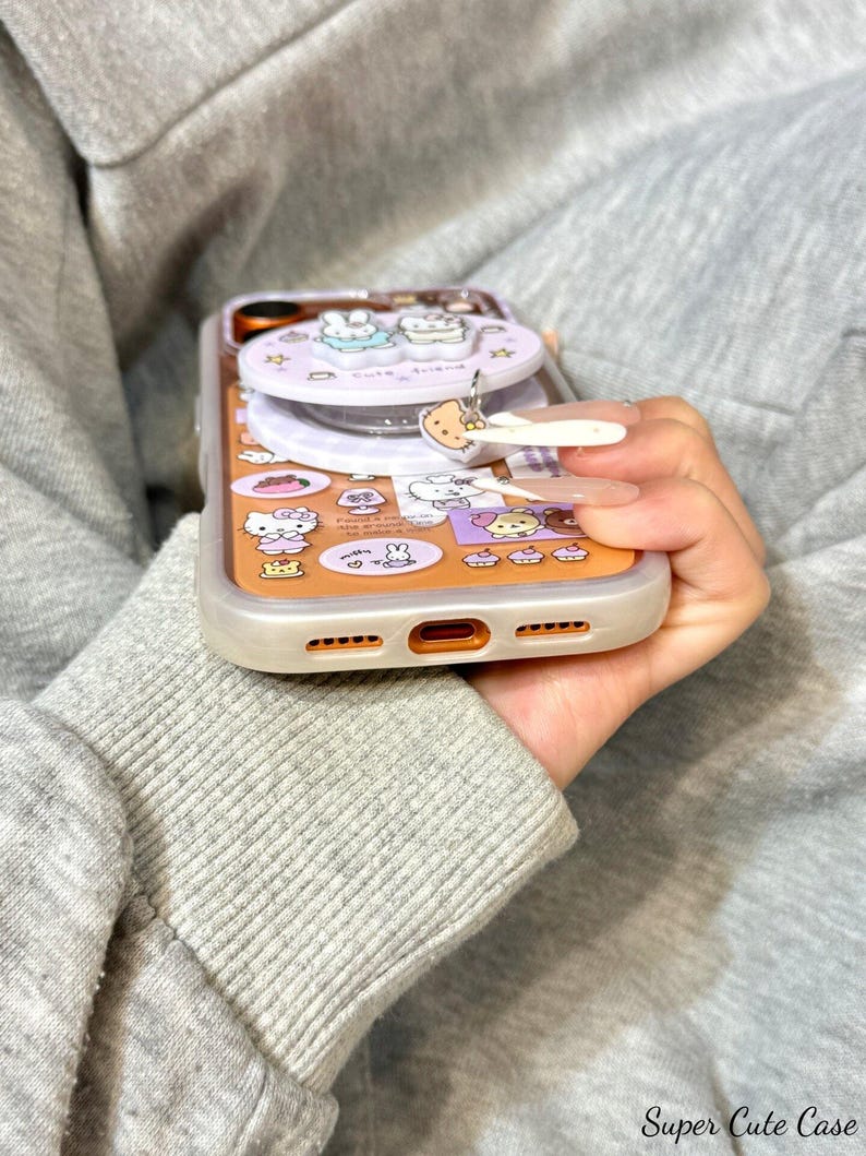 May include: A clear phone case with a cartoon design featuring a variety of characters and shapes in orange, pink, and white. The case has a pop-up feature and a charm. The text "Super Cute Case" is visible at the bottom.