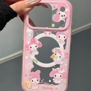 May include: Pink phone case with a clear center and a pink border. The case is decorated with cartoon characters, strawberries, and musical notes. The text "My Melody" is printed on the case.