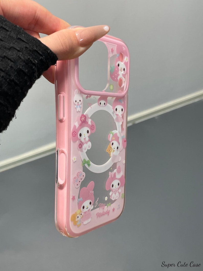 May include: Pink phone case with a clear center and a design featuring cartoon characters, strawberries, and stars. The case has a pink border and the words "Love Melody" are printed on the front. The case is held by a hand.