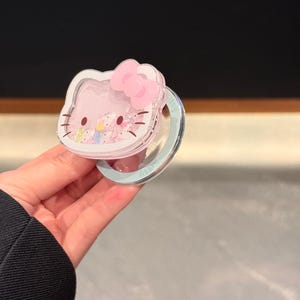 May include: A pink Hello Kitty-shaped phone case with a clear, glitter-filled center and a pink bow. The case is held in a hand. The text "Super Cute Case" is visible in the bottom right corner.